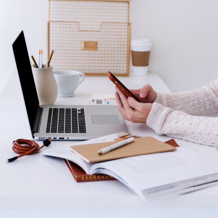 woman working on her computer while checking her phone